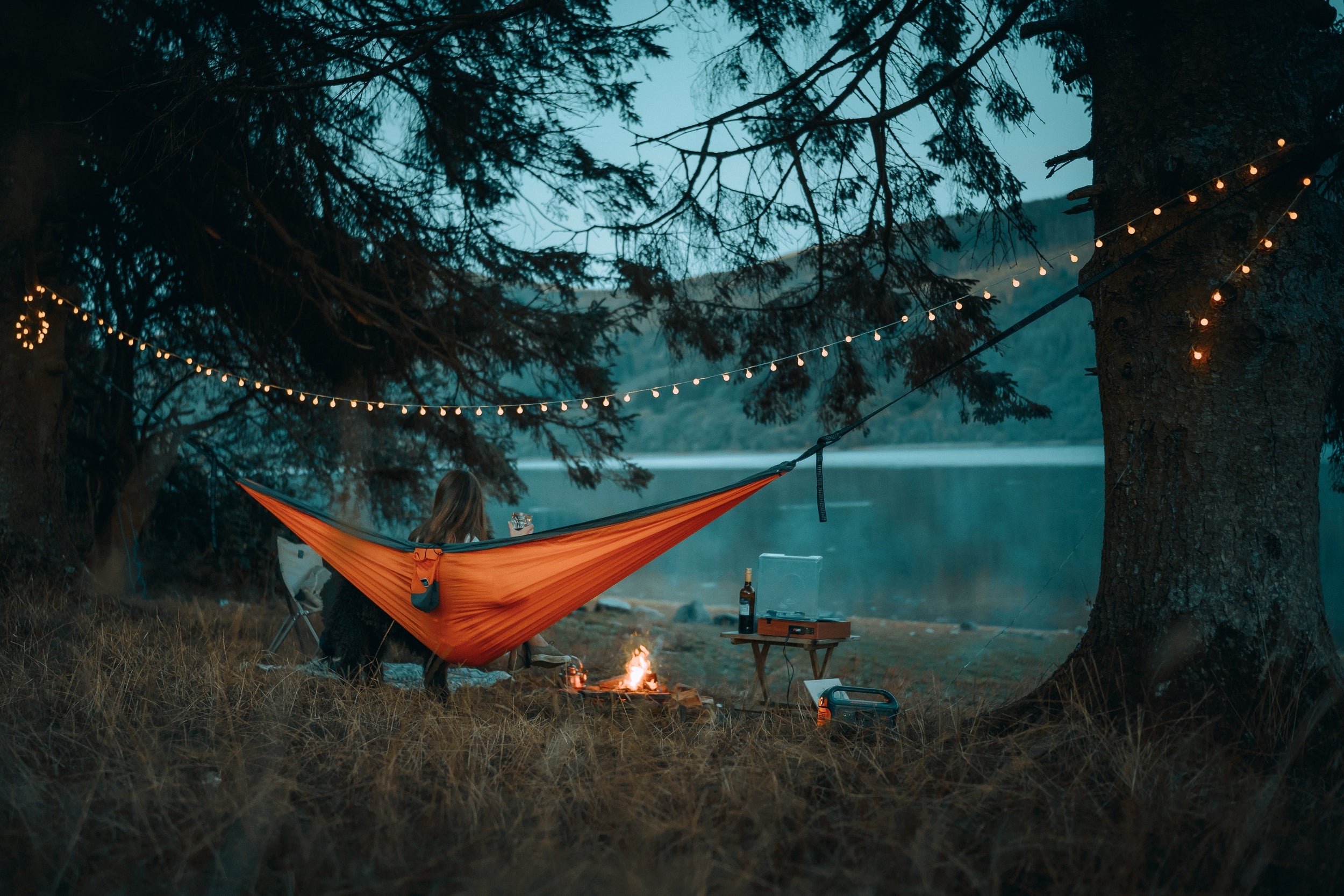 Woman relaxing in a Nakie hammock strung between two trees at dusk.