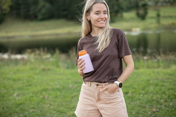 Dusty pink insulated coffee cup with orange lid, held by woman wearing brown t-shirt outdoors