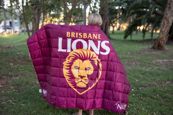Brisbane Lions maroon quilted puffy blanket with white text, yellow lion logo, displayed outdoors on person's shoulders