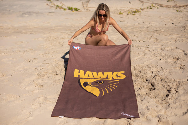 Brown beach towel with yellow Hawks logo and AFL branding, displayed on sand