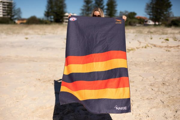 Adelaide Crows navy beach towel with horizontal orange and gold stripes, held up on beach