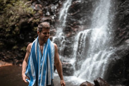 Image of a man with Nakie's recycled sand-free beach towel draped around his neck, enjoying comfort and convenience during his beach outing.
