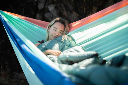 Woman enjoying a cozy moment in a Nakie hammock wrapped in a puffy blanket, showcasing the warmth and comfort of the blanket, perfect for chilly outdoor evenings