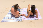 Image of a couple holding hands while relaxing on Nakie's couple combo recycled sand-free beach towel, enjoying a sustainable and romantic beach experience together. preview #5