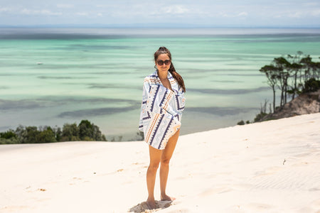 Image of a woman wrapped in Nakie's recycled sand-free beach towel, enjoying comfort and sustainability during her beach outing.
