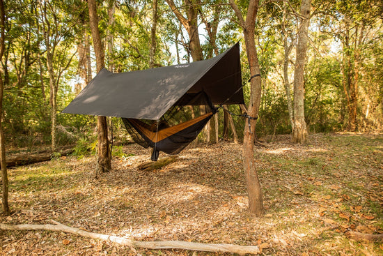 Nakie hammock with bug net and rain tarp between trees at a forest campsite. 
