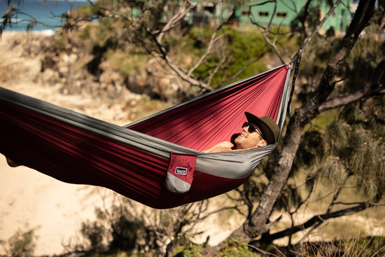 Person relaxing in a Nakie Merlot Red hammock in a forest.