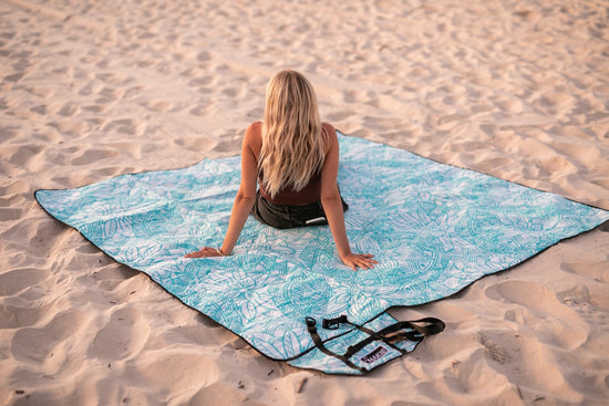 Woman siting on a Nakie Floating Lotus picnic blanket at the beach.