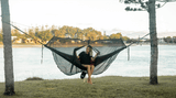 Woman in a Nakie hammock with a bugnet relaxing by the water. Nakie - Australia
