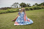 Sustainable down puffy blanket in blue, coral and white geometric print, shown draped over person sitting on grass preview #5