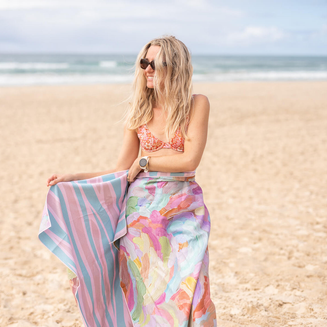 Recycled sand-free beach towel with pink striped and floral watercolor pattern, displayed on beach