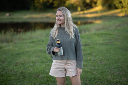 Classic Silver cooler and coffee cup in use, held by woman wearing gray ribbed sweater and cream shorts outdoors
