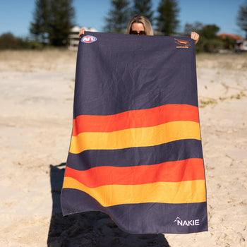 Adelaide Crows navy beach towel with horizontal orange and gold stripes, held up on beach
