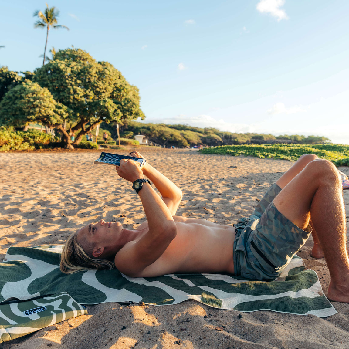 Eucalyptus green and white zebra-stripe beach towel spread on sand with person reading on it