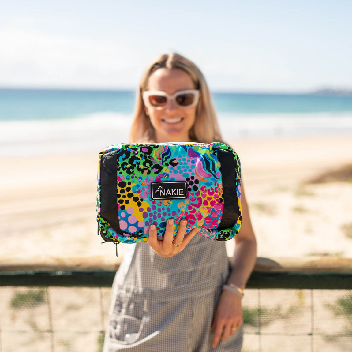 Colorful abstract patterned recycled tote bag with black panels and Nakie label, held at beach