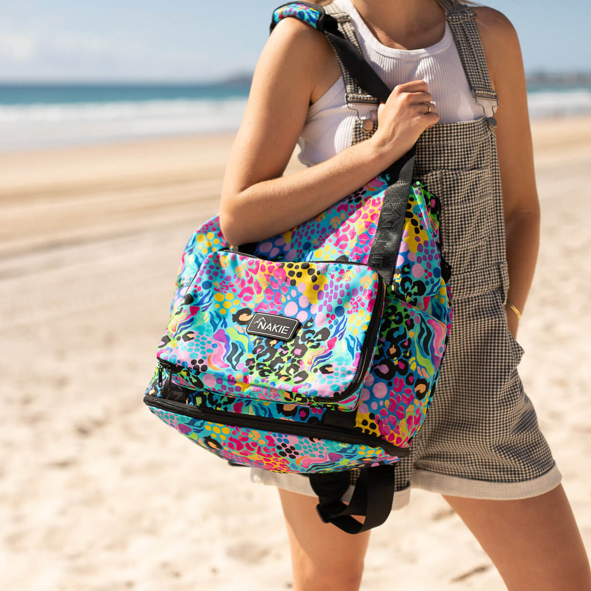 Kasey Rainbow recycled tote bag with multicolour abstract pattern and black trim, worn on shoulder at beach