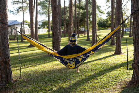 Back view of person sitting in a Nakie NRL Cowboys hammock between trees in a park