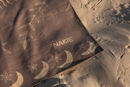 Brown recycled beach towel with gold moon and star pattern, displayed on sand