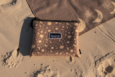 Brown recycled nylon pouch with celestial moon and sun pattern, black zipper and NAKIE brand label, displayed on sand.