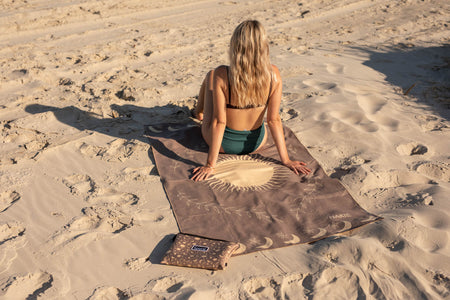 Luna Glow recycled sand-free beach towel in taupe with celestial print, laid on sand beach