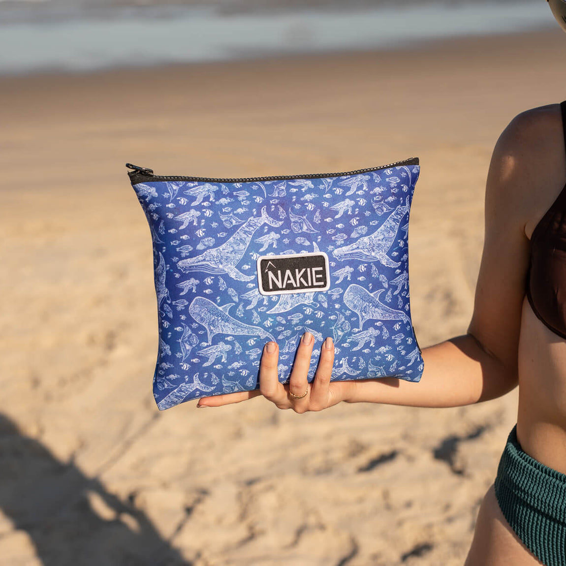 Blue recycled sand-free beach towel with underwater sea creature print, held by woman at beach