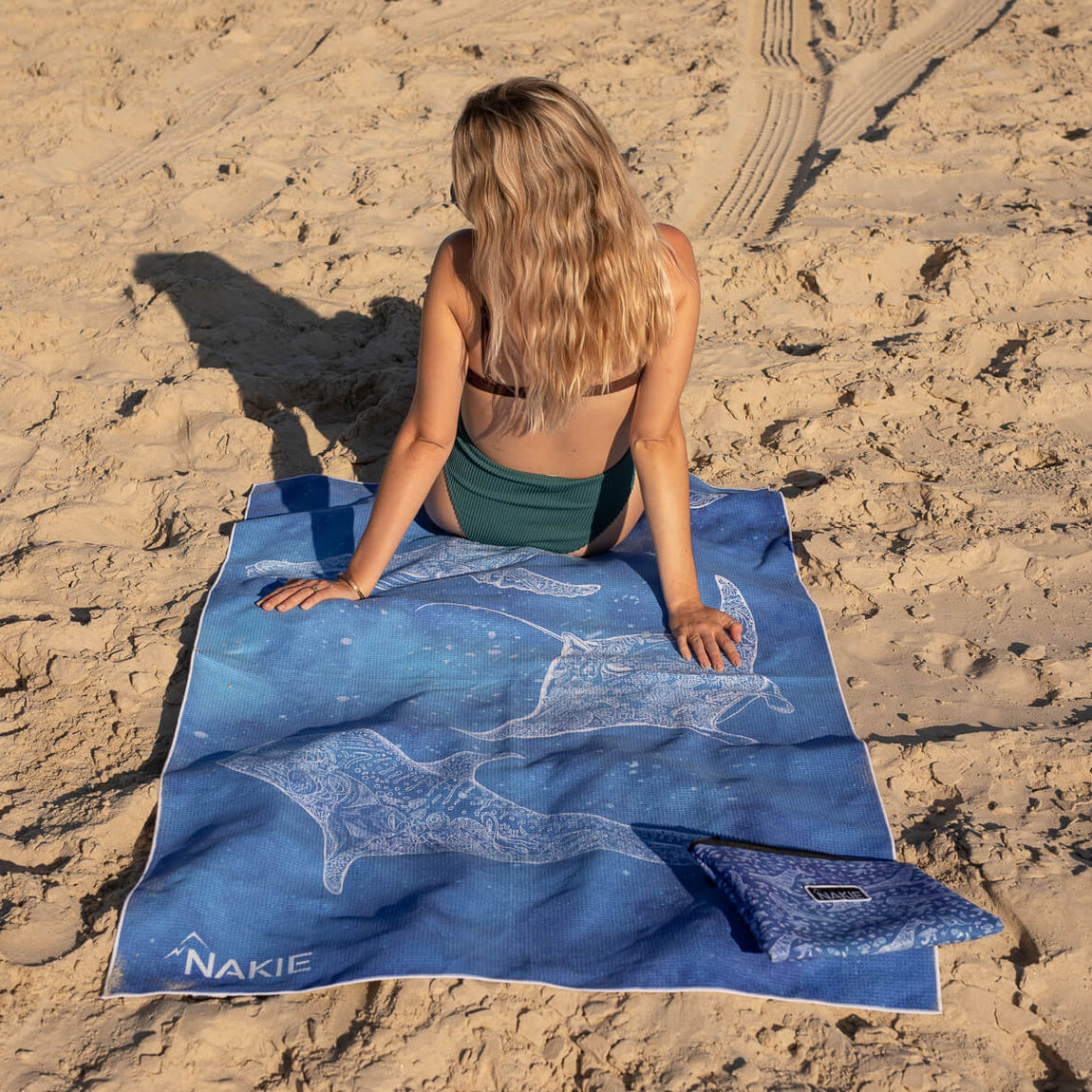 Blue recycled beach towel with white whale and sea creature designs, displayed on sand.