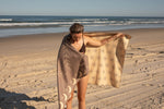 Beige recycled beach towel with moon and star print, displayed on beach by woman wrapping around shoulders preview #10