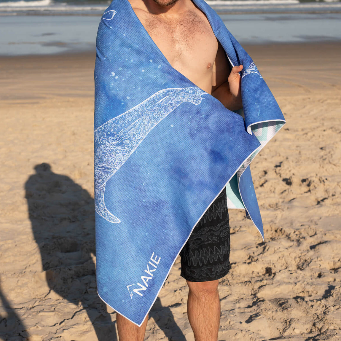 Blue beach towel with white wave design, sand-free texture, worn by man on sandy beach