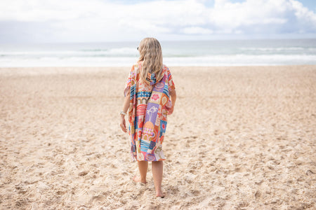 Colorful retro geometric hooded towel worn on beach, back view, showing vibrant multi-colored patchwork pattern.