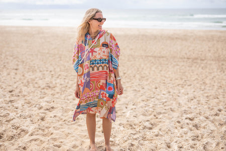 Colorful hooded towel with retro beach-inspired geometric print in red, blue, orange and purple, worn on beach.