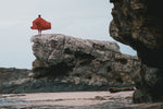 A man draping Nakie's Earth Red Sustainable Down Puffy Blanket over her back while admiring the beach view. preview #12