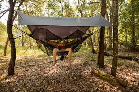A man lounging in a Nakie hammock shielded by our Bug Net & Rain Tarp Combo, ensuring a peaceful outdoor experience away from insects and rain.