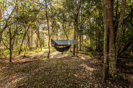 A scenic view of Nakie's Bug Net & Rain Tarp Combo fully set up at a campsite, offering complete protection and comfort for outdoor enthusiasts.