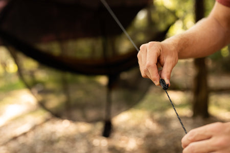 A man effortlessly setting up pegs and guylines for Nakie's Bug Net & Rain Tarp Combo without the need for knots, ensuring quick and hassle-free assembly.