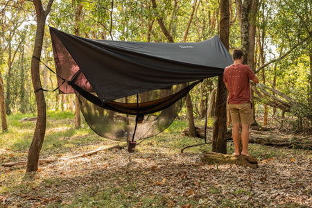 A man effortlessly setting up Nakie's Bug Net & Rain Tarp Combo, preparing for a comfortable and protected outdoor experience.