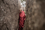 Image of a woman wrapped in Nakie's Earth Red Sustainable Down Puffy Blanket, enjoying warmth and sustainability during outdoor adventures. preview #8