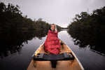 Image of a woman wrapped in Nakie's Earth Red Sustainable Down Puffy Blanket, sitting on a boat and enjoying warmth and sustainability during her maritime adventure. preview #3