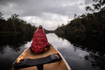 Image of a woman wrapped in Nakie's Earth Red Sustainable Down Puffy Blanket, sitting on a boat and enjoying warmth and sustainability during her maritime adventure. preview #11