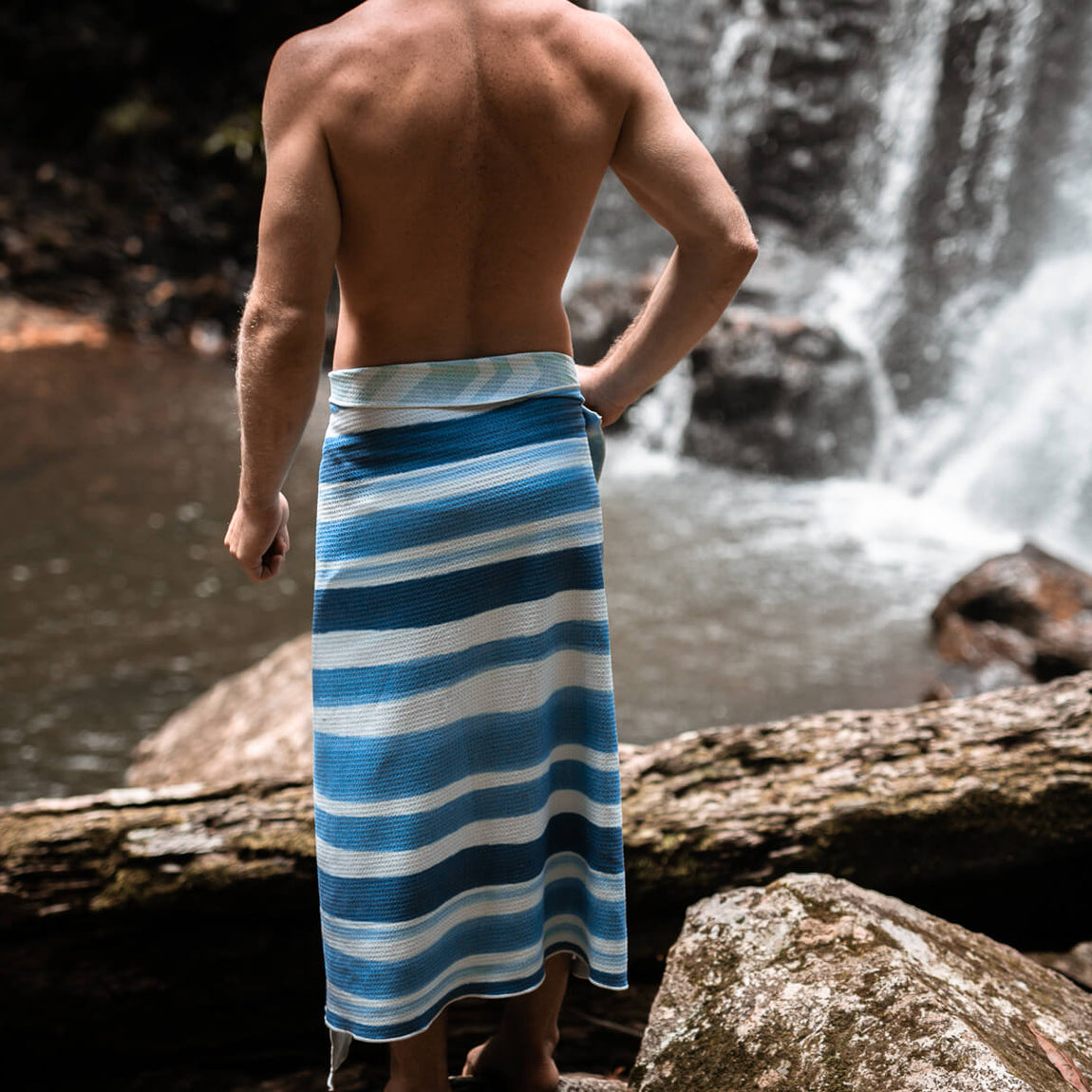 Blue and white striped recycled sand-free beach towel wrapped around man's waist by waterfall