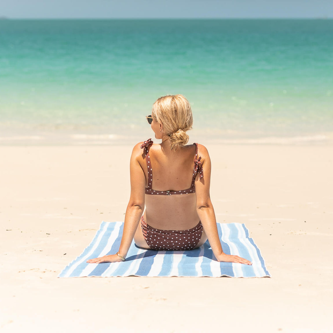 Blue and white striped recycled beach towel displayed on sand at the shore