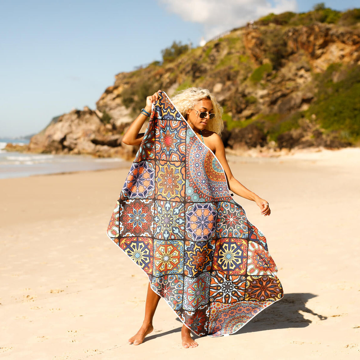 Recycled sand-free beach towel with multicolour geometric tile pattern, draped on woman at beach.